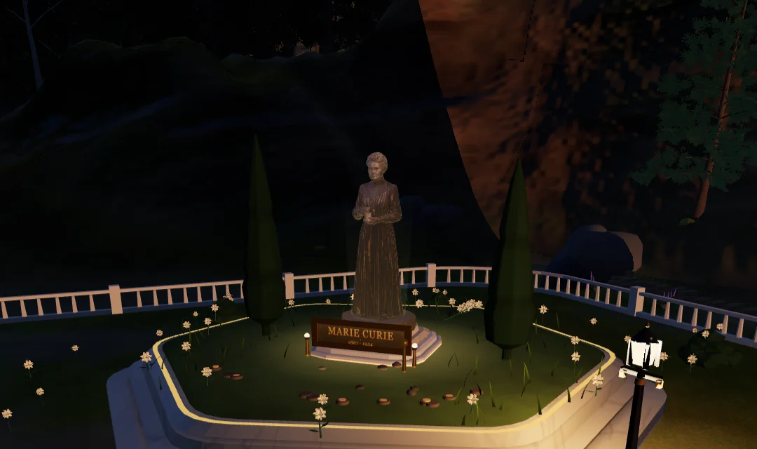 Curie's tribute plot in the Vale at golden hour: the statue over its garden, the lamps just lit